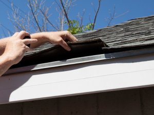 Roofer in Arkansas inspecting wind damage on a residential roof, fully secured and safety compliant.